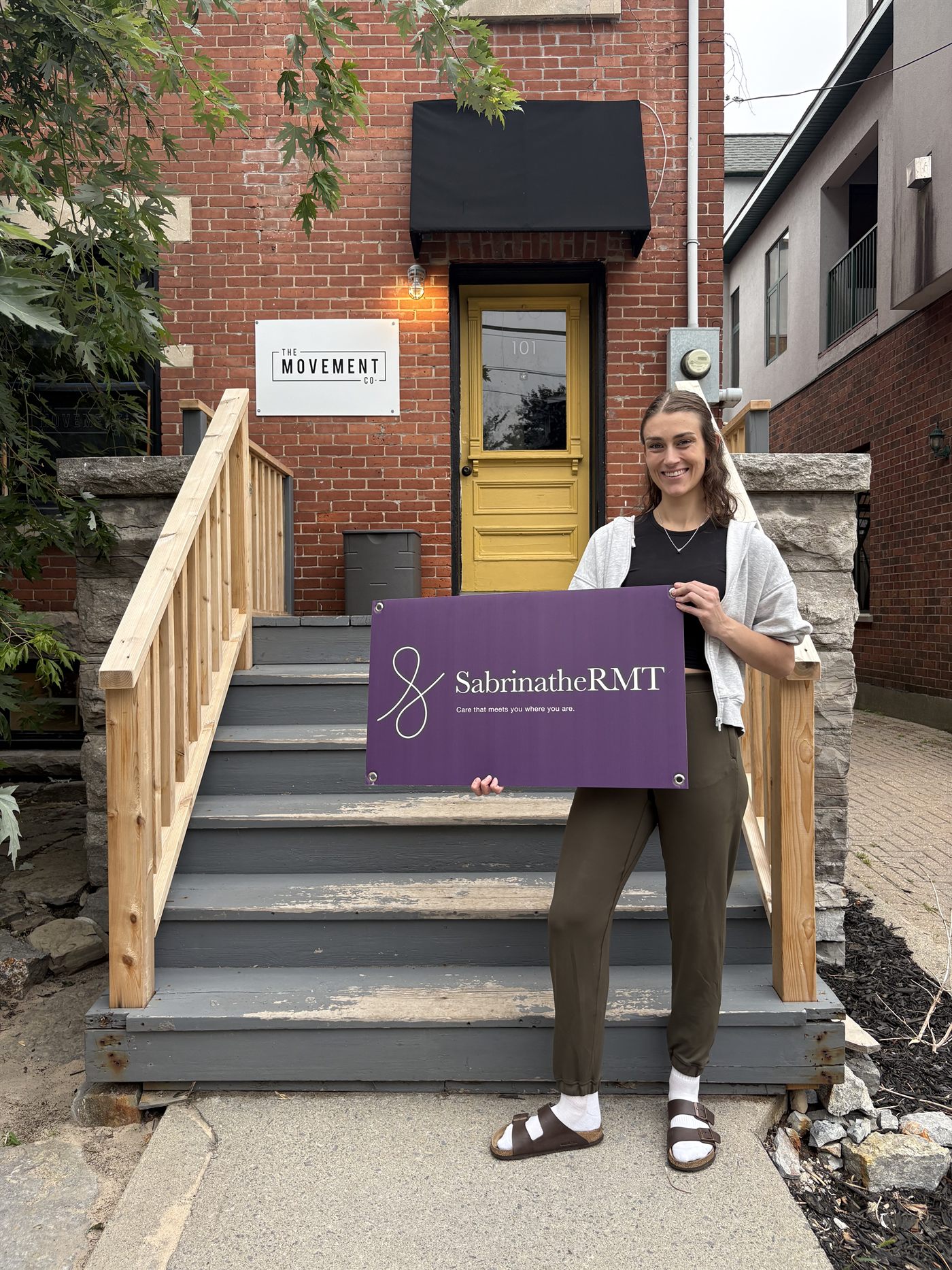 Sabrina at The Movement Co. entrance on Fourth Avenue with a Sabrina The RMT sign.